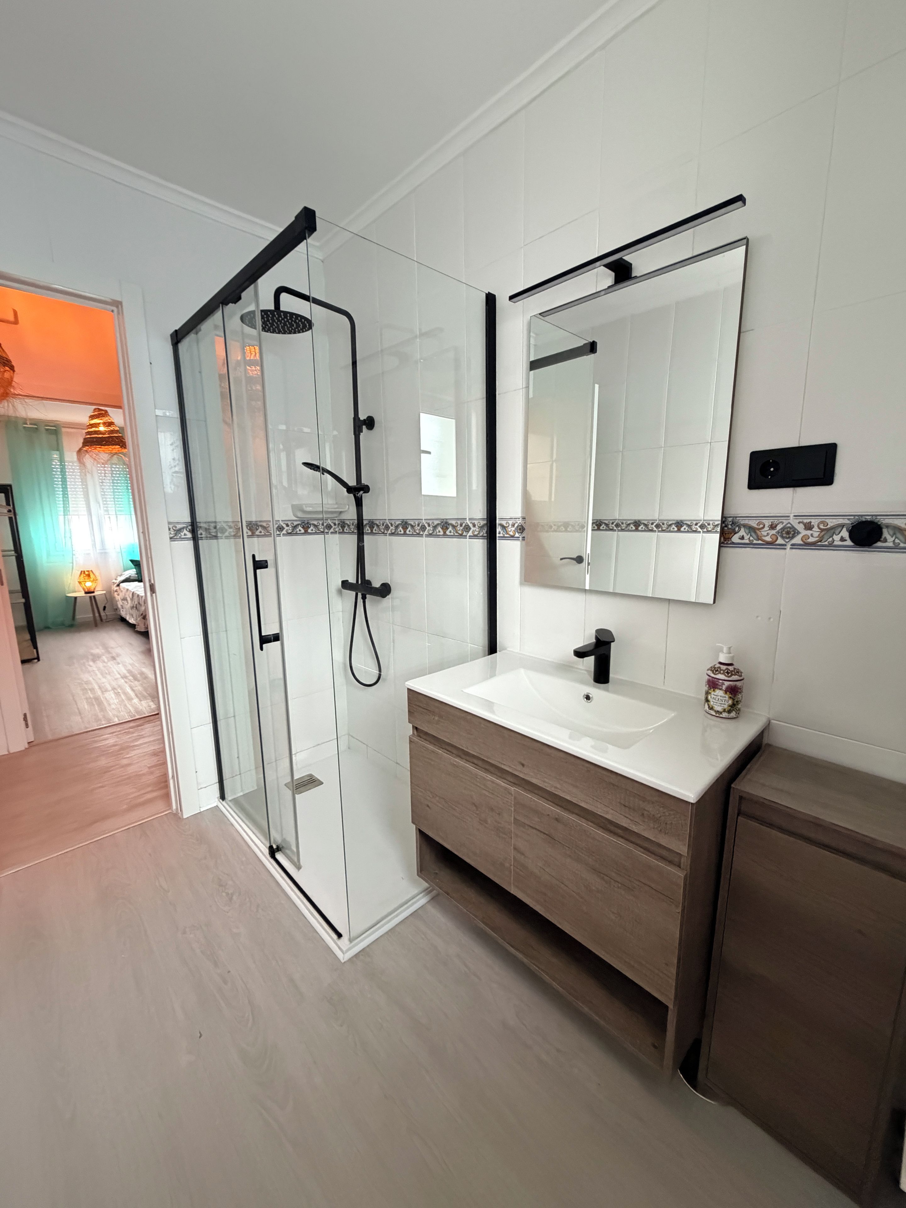 A modern bathroom with a glass-enclosed shower, a white sink with a wooden vanity, and a large mirror above the vanity.