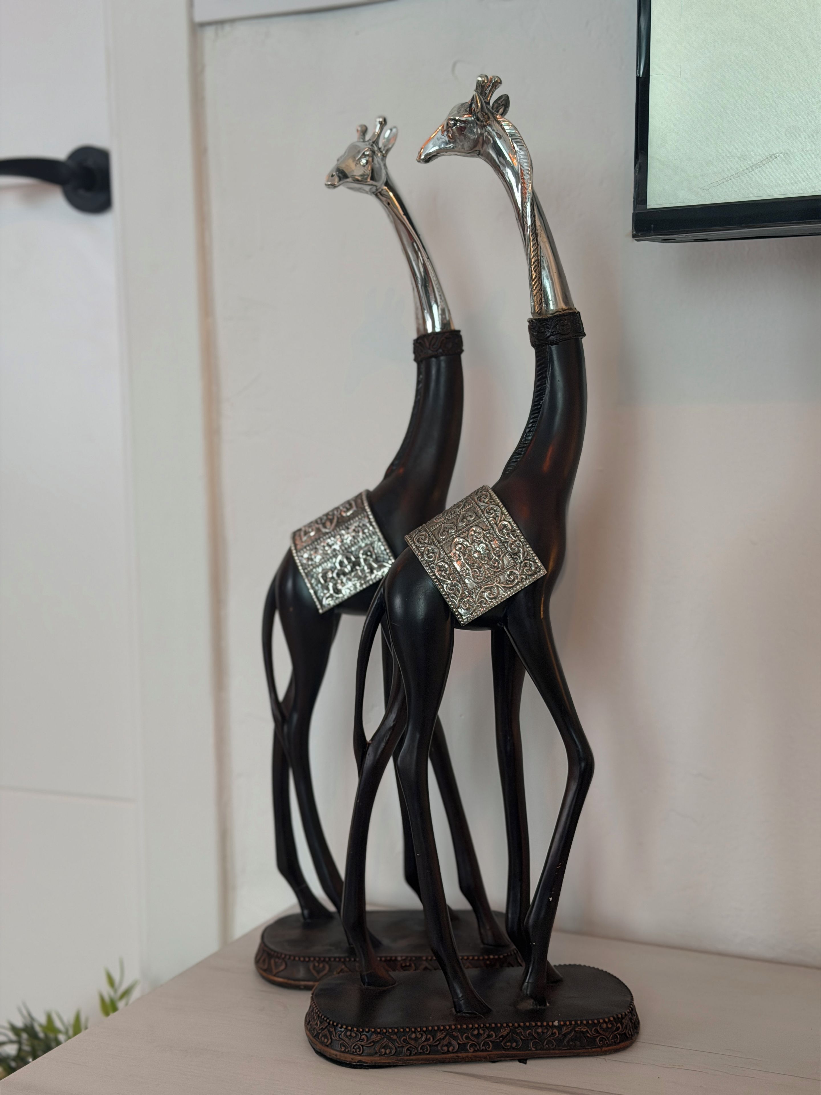 Dos esculturas decorativas de jirafas con diseños intrincados en sus bases, sobre una superficie plana.