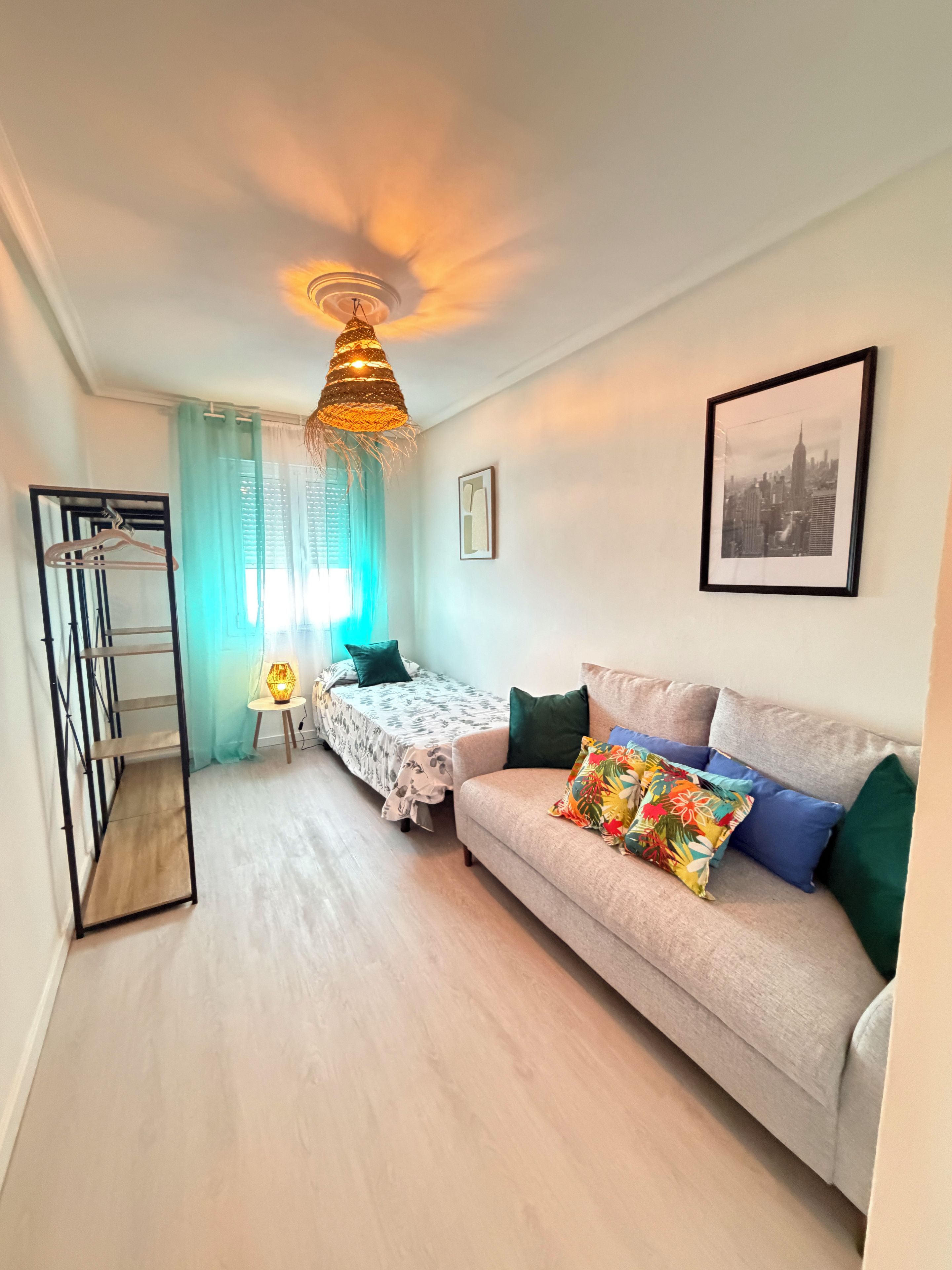 A cozy living room with a sofa, a bed, a hanging light fixture, and a framed picture on the wall.