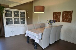 A dining area with a table set for four, a cabinet with glass doors, a wall-mounted lamp, and two decorative panels. - Bungalow with 1 bedroom (Westkapelle)
