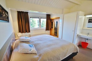 A hotel room with a bed, a window with curtains, a bathroom with a sink, and a door leading to another room. - Bungalow with 1 bedroom (Westkapelle)