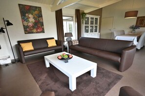 Een woonkamer met een bruine bank, een witte salontafel en een schilderij aan de muur.
