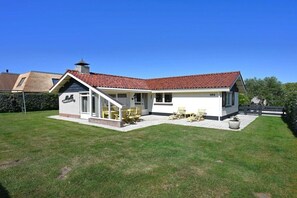 A two-story house with a red-tiled roof, a chimney, and a white exterior. There is a covered patio with outdoor furniture. - Bungalow with 1 bedroom (Westkapelle)