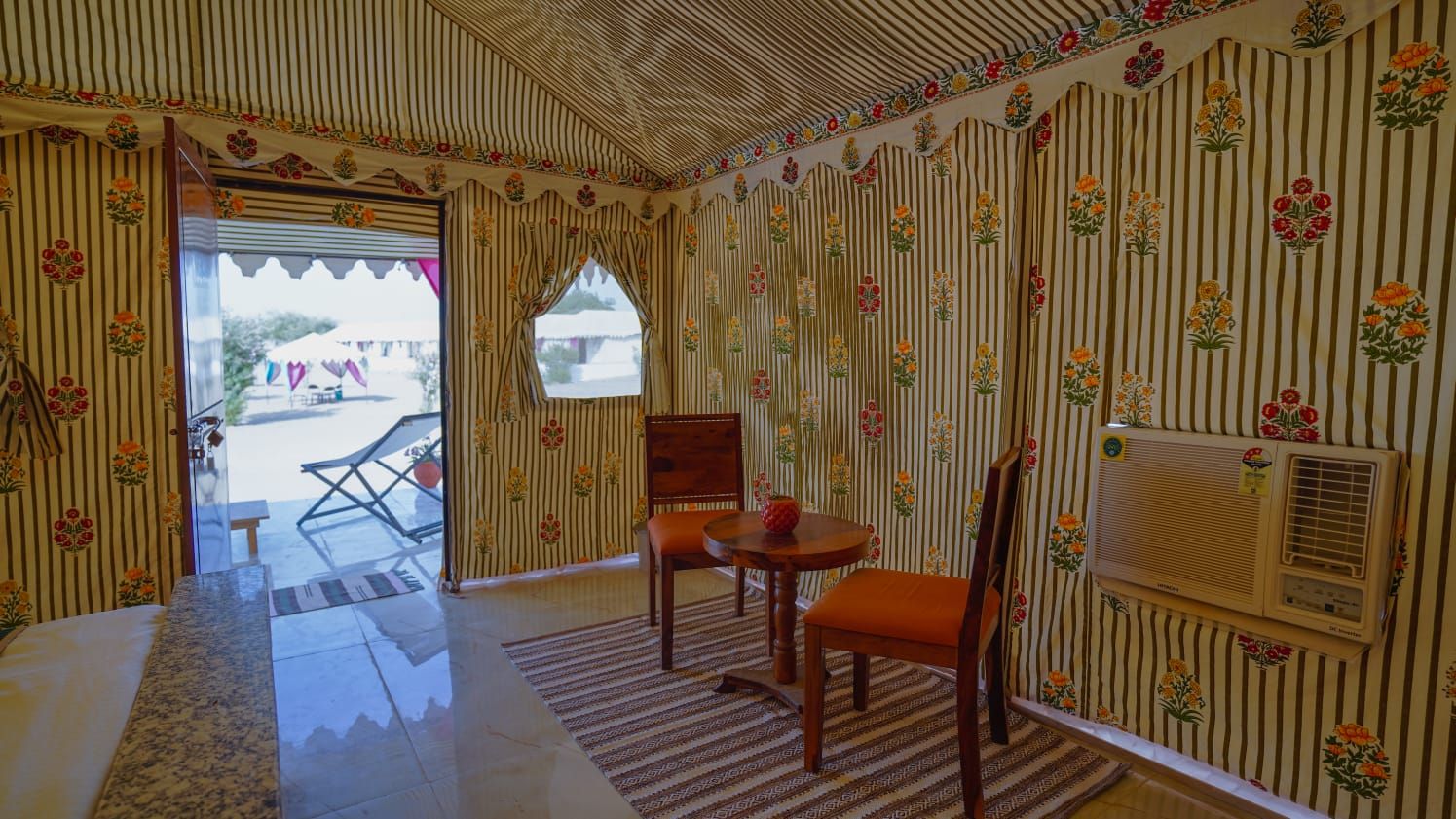 Ein Zimmer mit Streifenmuster-Tapete, einem Holztisch mit Stühlen, einem Fenster und einer Klimaanlage.