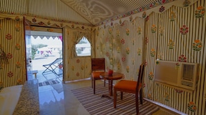 A room with striped wallpaper, a wooden table with chairs, a window, and an air conditioning unit. - Desert Walk Camp (Jaisalmer)