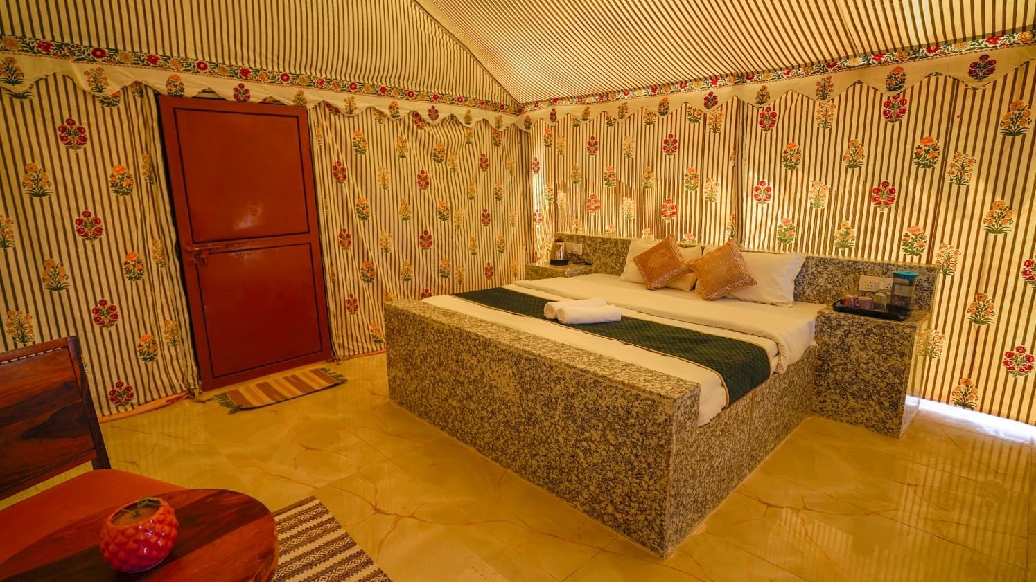 Quarto com cama, mesa de cabeceira, guarda-roupa vermelho e papel de parede estampado.