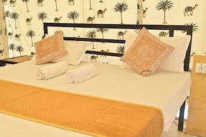 A neatly made bed with two pillows and two rolled towels, a wooden headboard, and a patterned wall. - Desert Walk Camp (Jaisalmer)