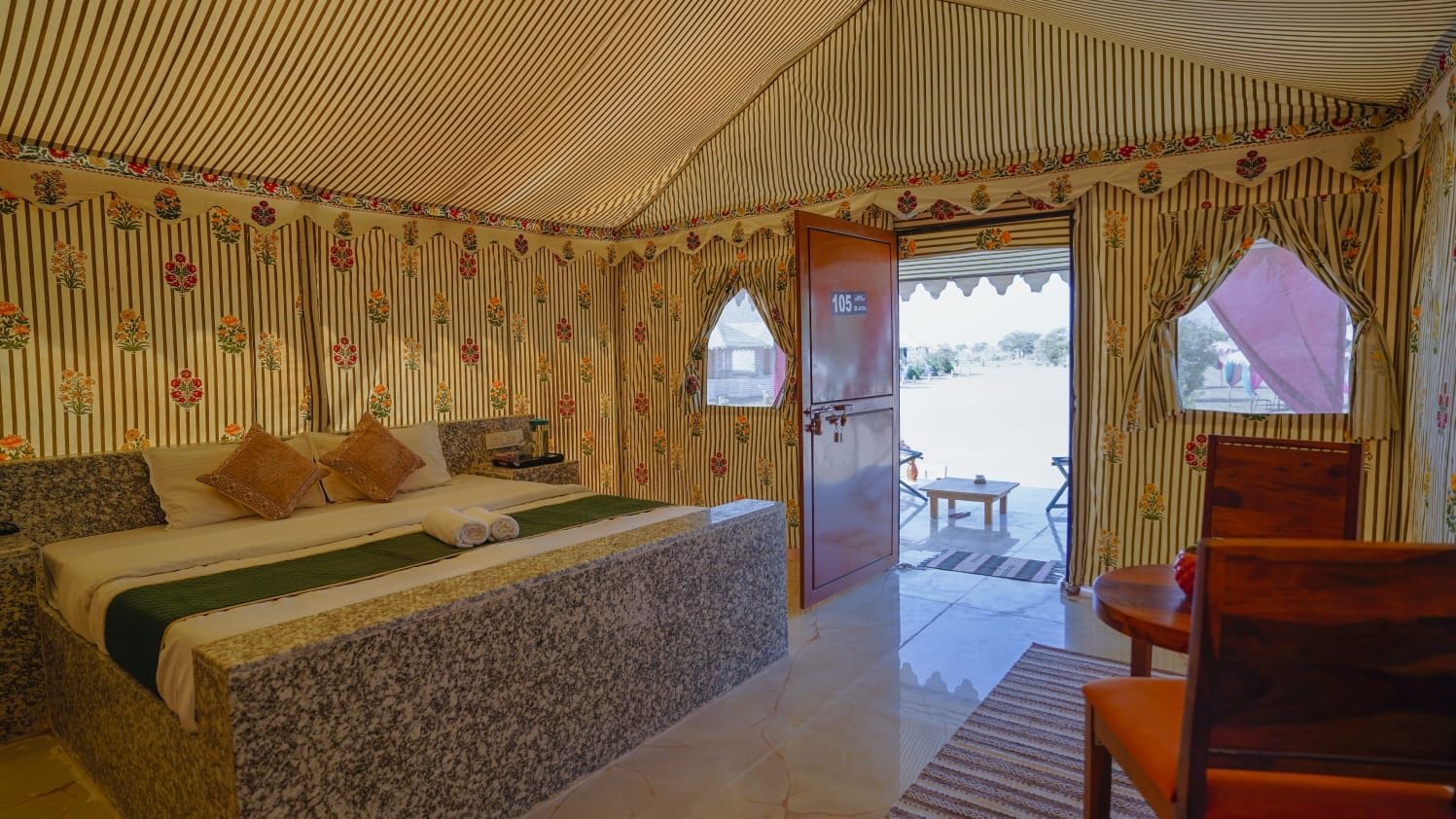 Quarto com cama, cadeira de madeira e janela com cortinas.