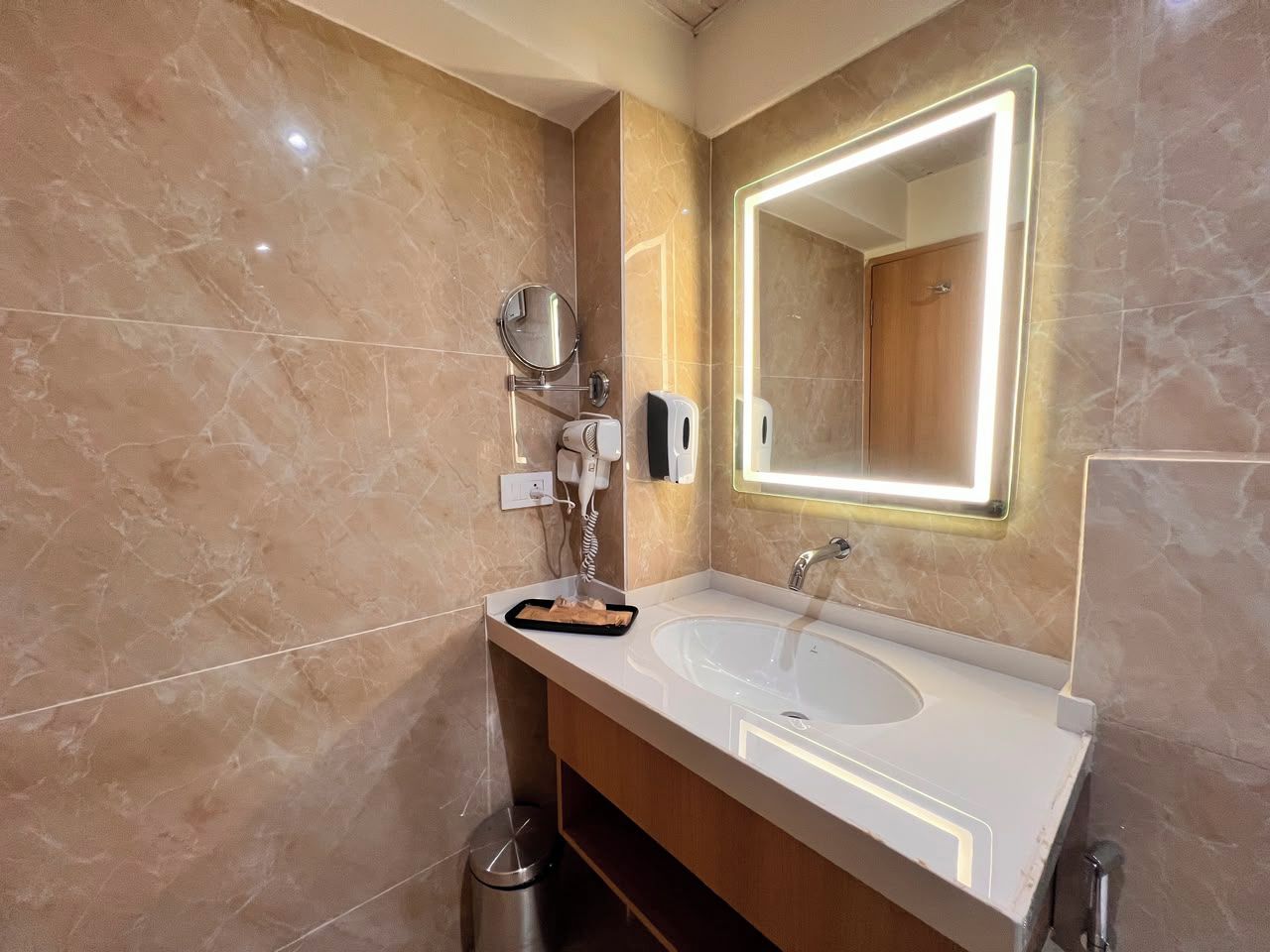 Un baño moderno con tocador de mármol, un espejo grande con iluminación perimetral y un secador de pelo de mano.