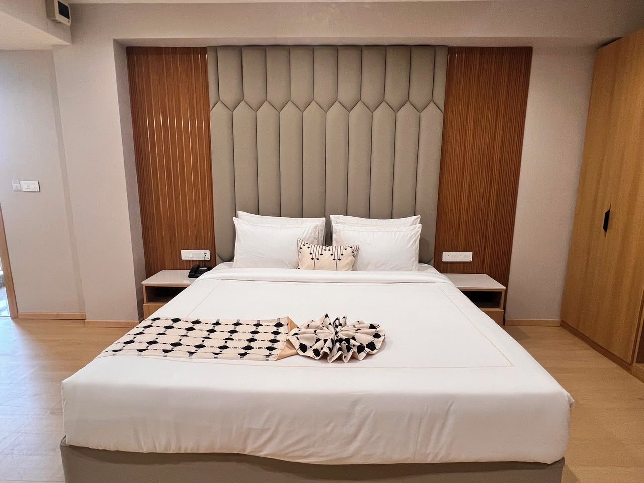 Una habitación de hotel con una cama grande, un cabecero de estampado geométrico, dos mesitas de noche y un armario de madera.