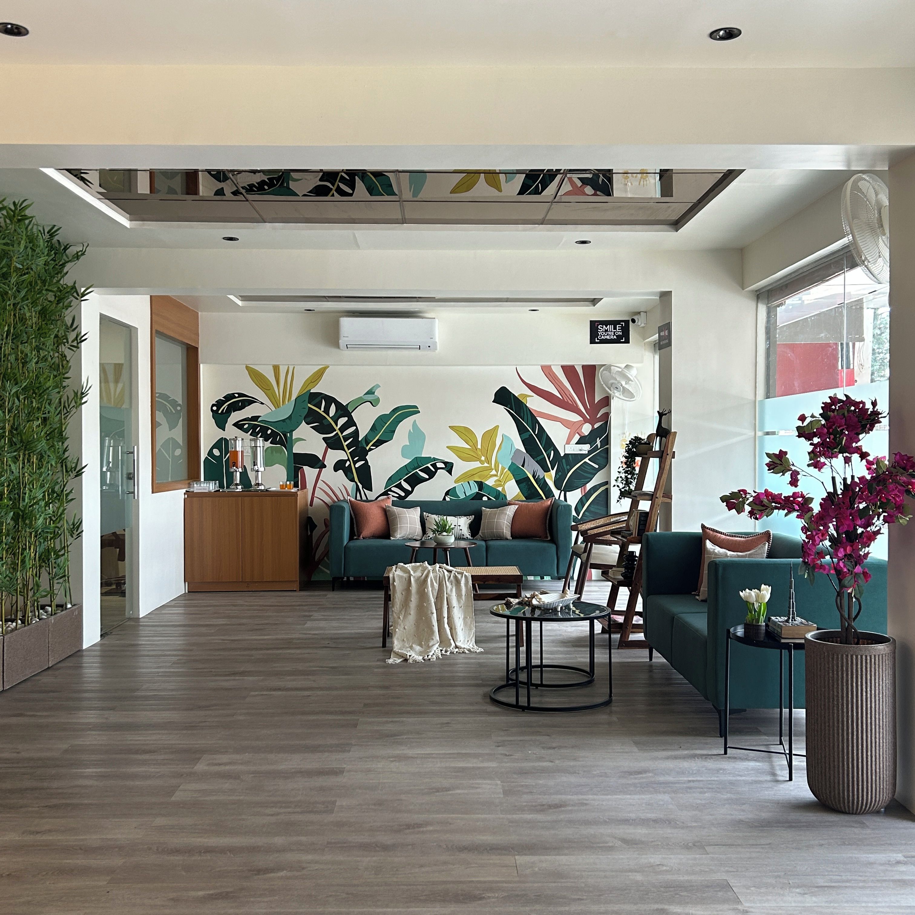 Una sala de estar moderna con un mural tropical grande, un conjunto de sofás, una mesa de centro y una planta en maceta.