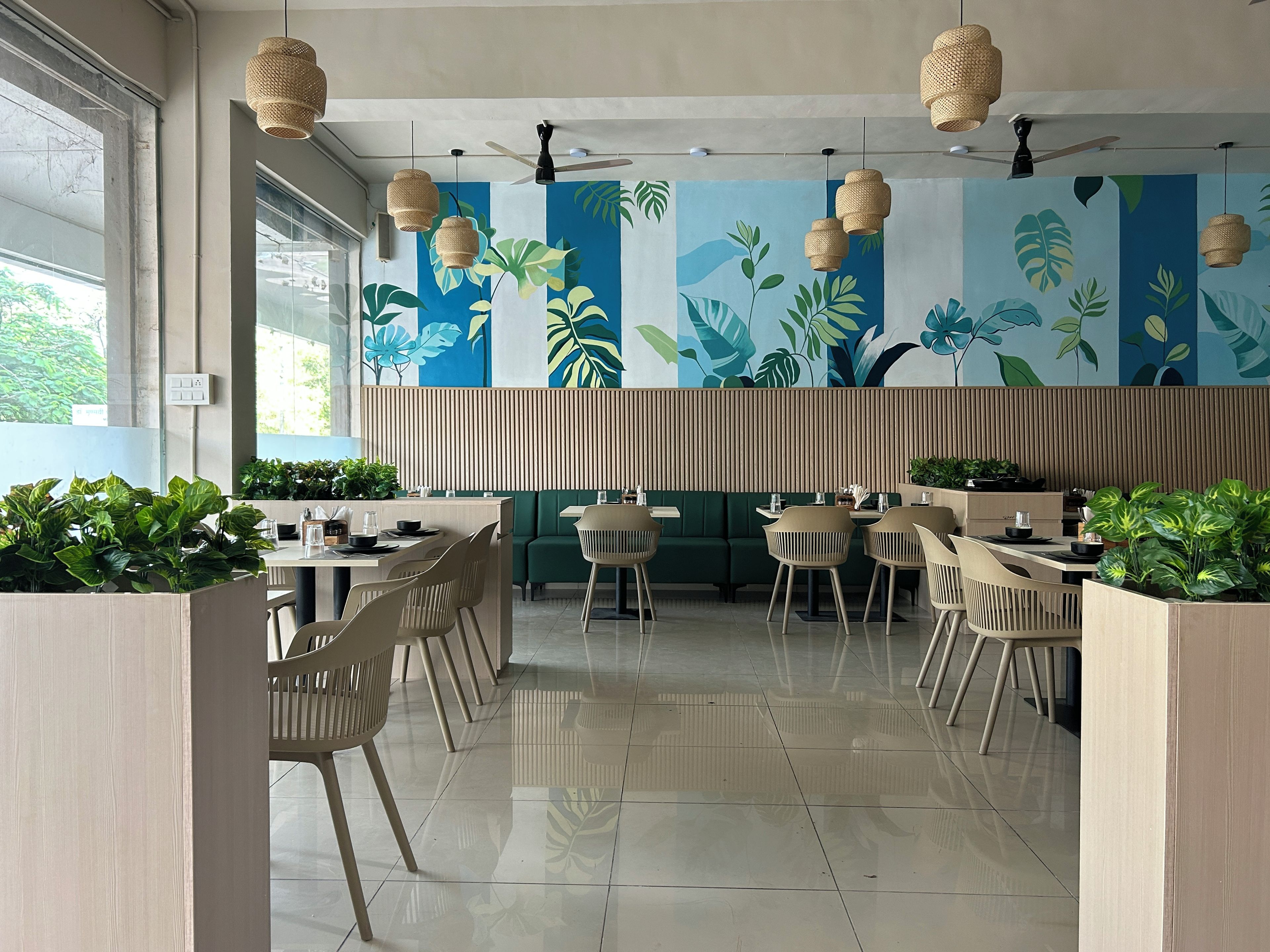 Interior de restaurante moderno con techos altos, ventiladores de techo y un mural tropical vibrante.