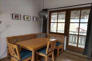 Un espace repas comprenant une table et des chaises en bois, un banc et une grande fenêtre donnant sur l’extérieur.