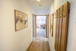 A hallway with a wooden floor, a framed picture on the left, and a wooden panel with hooks on the right. - Holiday apartment with 1 bedroom (Bad Hindelang)