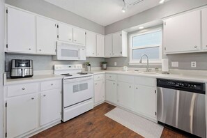 A modern kitchen with white cabinets, stainless steel appliances, and a wooden floor. - Miramar Beach | Beach Access & Fire Pit (Miramar Beach)