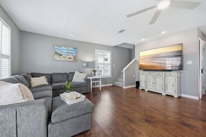 A spacious living room with a gray sectional sofa, a white coffee table, and a painting of a beach scene. - Miramar Beach | Beach Access & Fire Pit (Miramar Beach)
