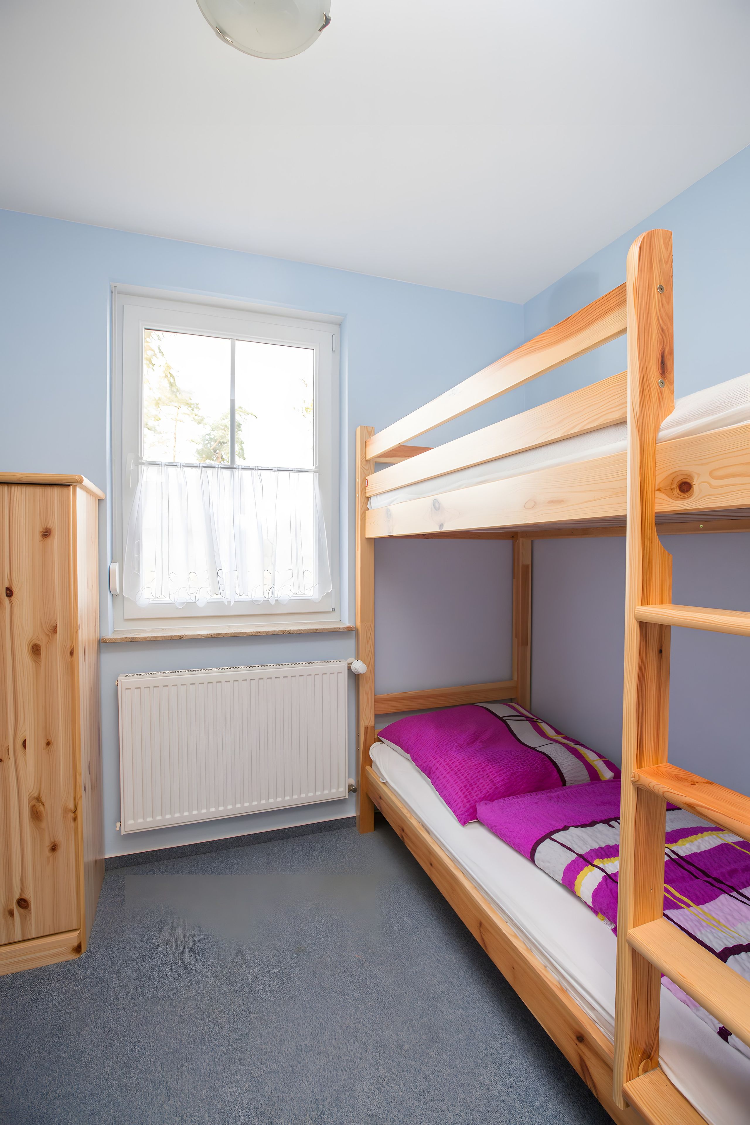 A bunk bed room with a window, radiator, and wooden furniture.