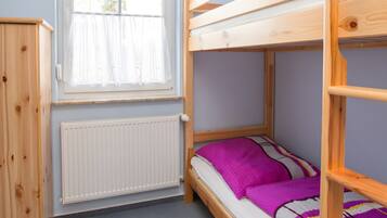 A bunk bed room with a window, radiator, and wooden furniture.