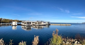 A docked houseboat with a covered deck and a small cabin, surrounded by calm water and a clear sky. - Apartment 'U 2 EG Otter' with sea view, private terrace and Wi-Fi (Röbel/Müritz)