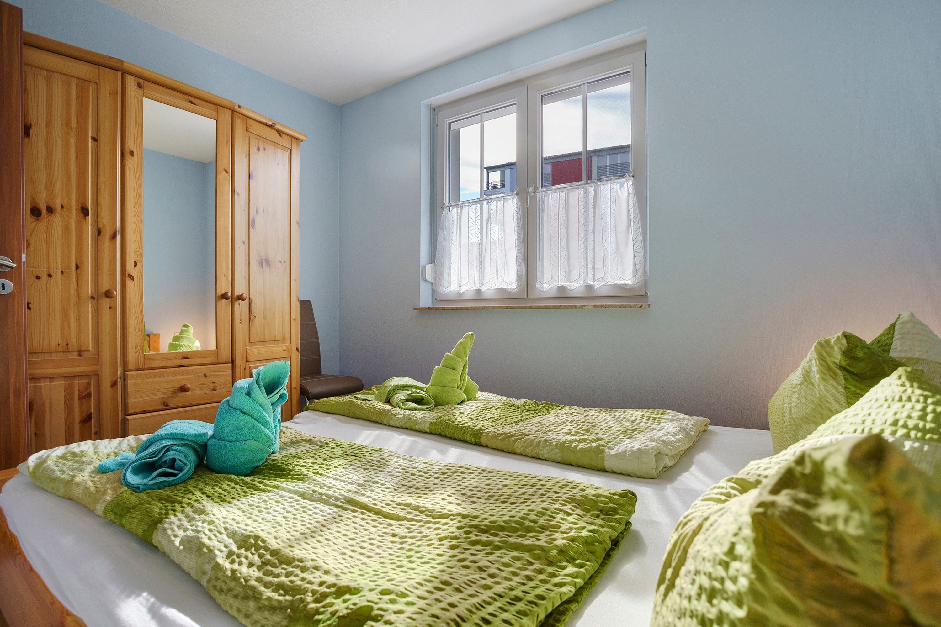A bedroom with a bed, a wooden wardrobe, and a window.