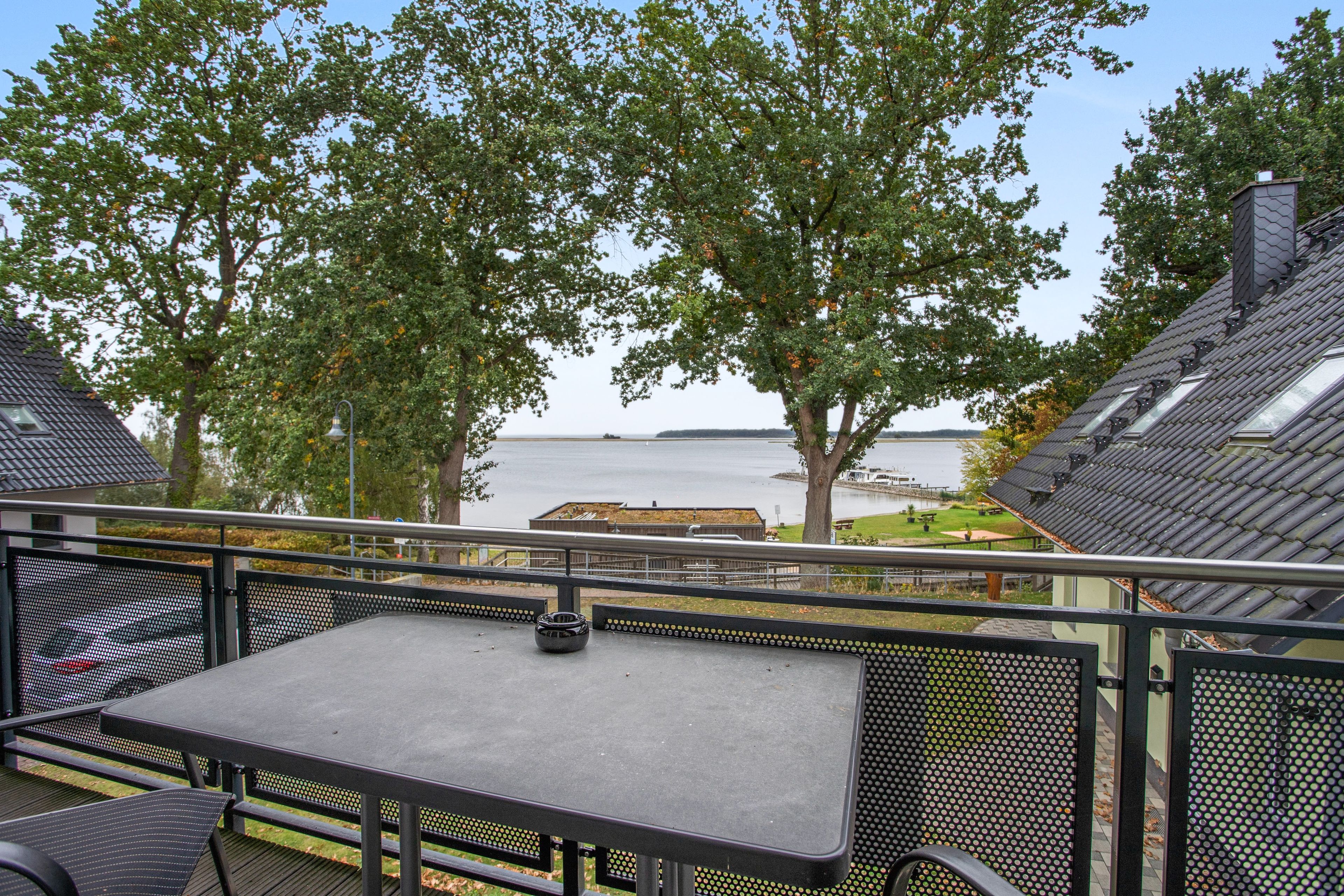 A terrace with a table and chairs, overlooking a body of water and trees.