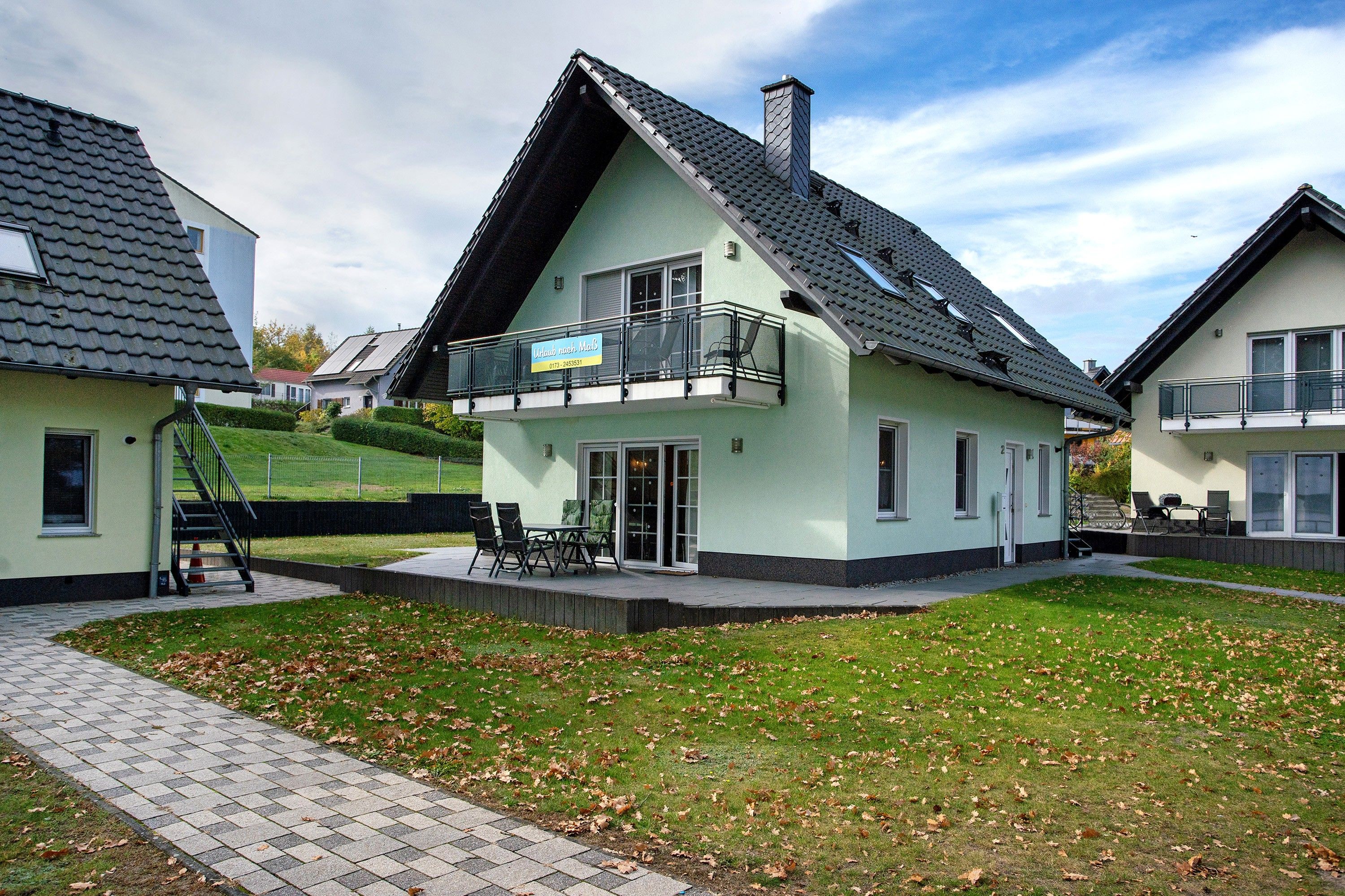 A two-story house with a balcony, a paved patio, and a grassy yard.