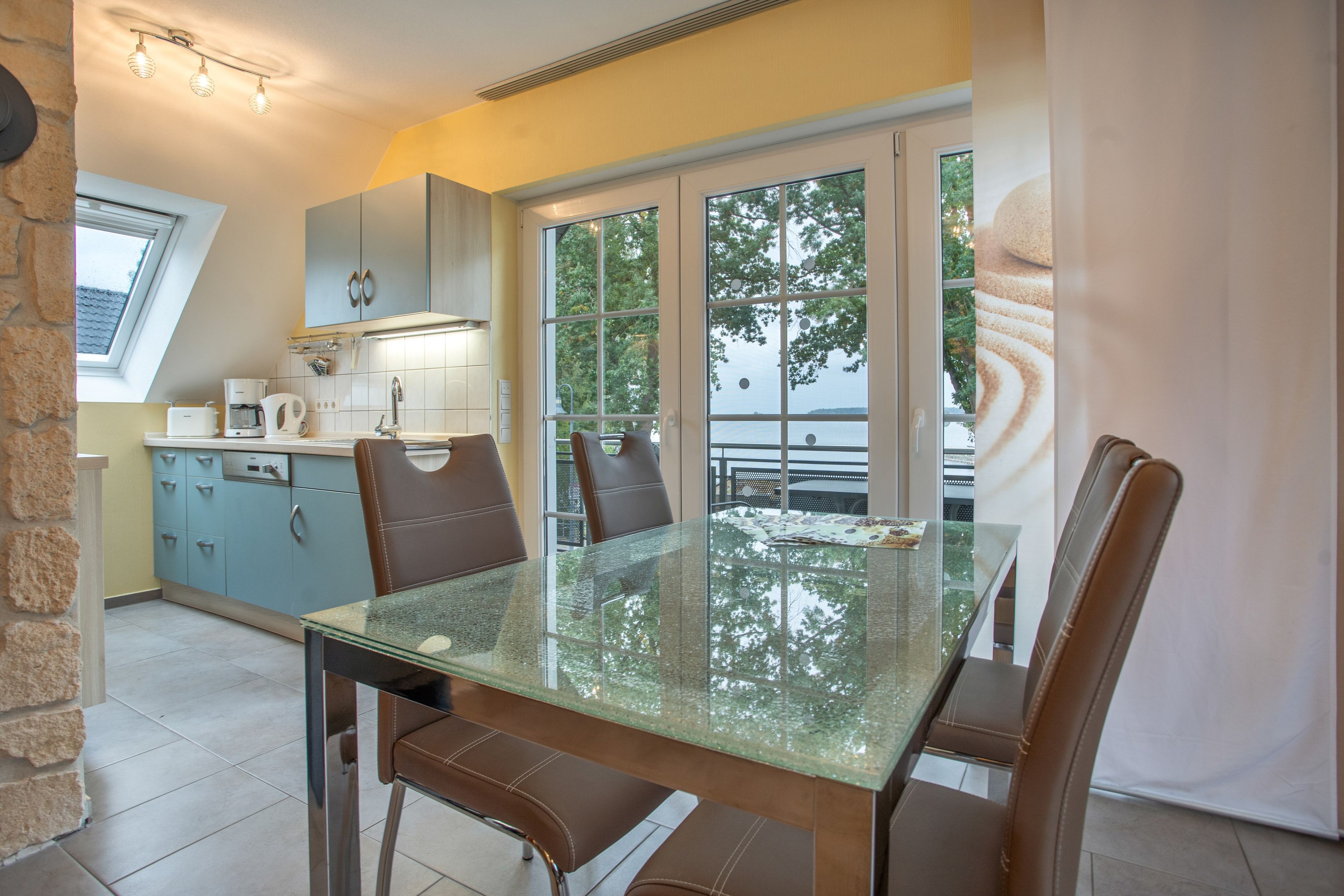 Een moderne keuken met een eethoek, met een tafel met glazen blad en bruine lederen stoelen.