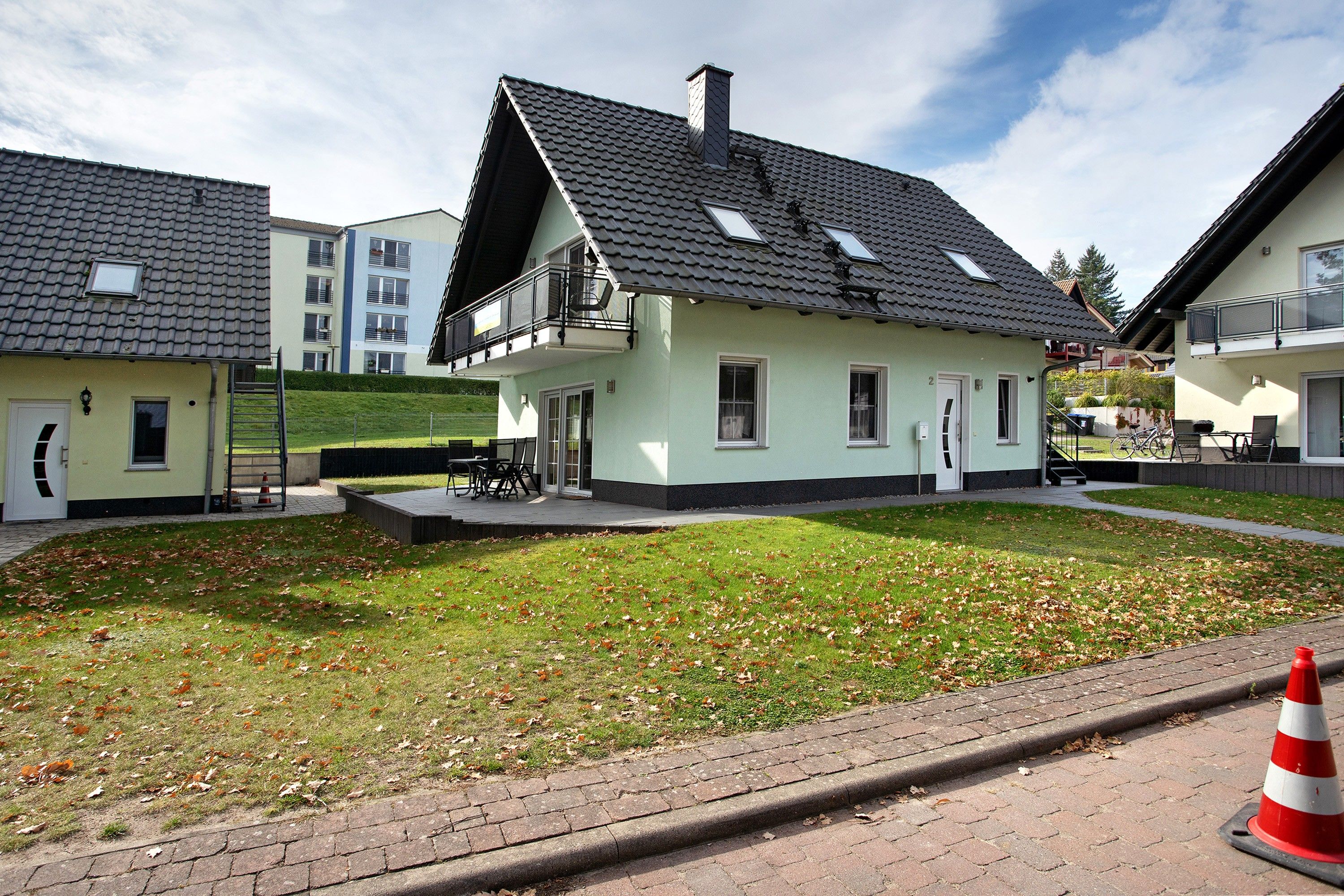 Ein Wohngebäude mit Satteldach, einem Balkon und einem kleinen Vorgarten mit Gras und herabgefallenen Blättern.