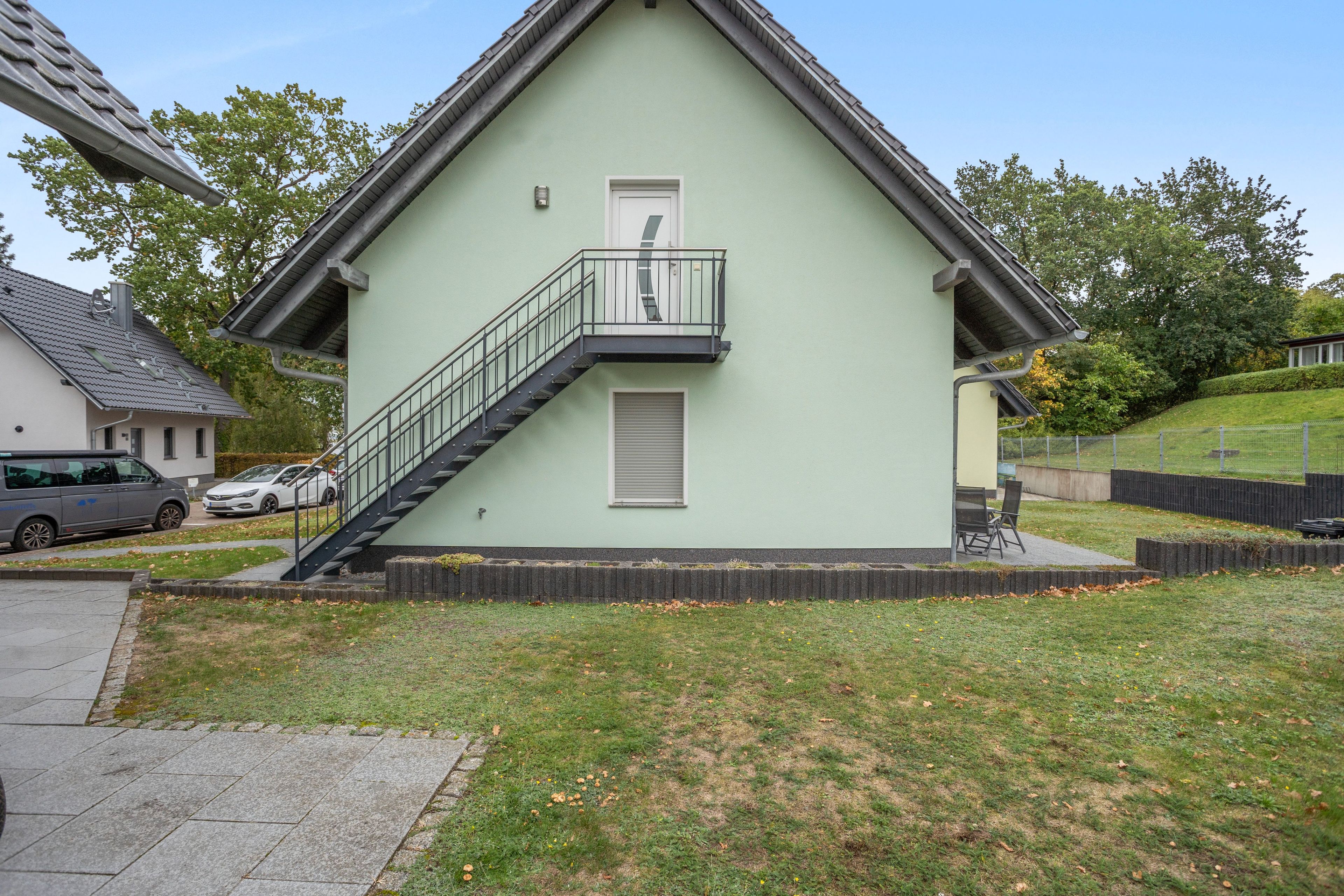 Ein zweistöckiges Gebäude mit Balkon, Treppe und kleinem Garten.