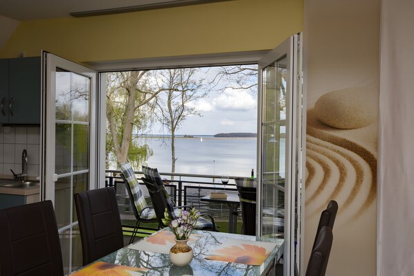 A dining area with a table, chairs, and a view of the water. - Apartment 'Haus U 2 OG Dachs' with Sea View, Shared Terrace and Wi-Fi (Röbel/Müritz)