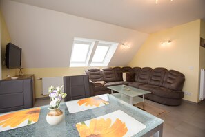 A modern living room with a sectional sofa, a flat-screen TV mounted on the wall, and a dining area with a glass table. - Apartment 'Haus U 2 OG Dachs' with Sea View, Shared Terrace and Wi-Fi (Röbel/Müritz)