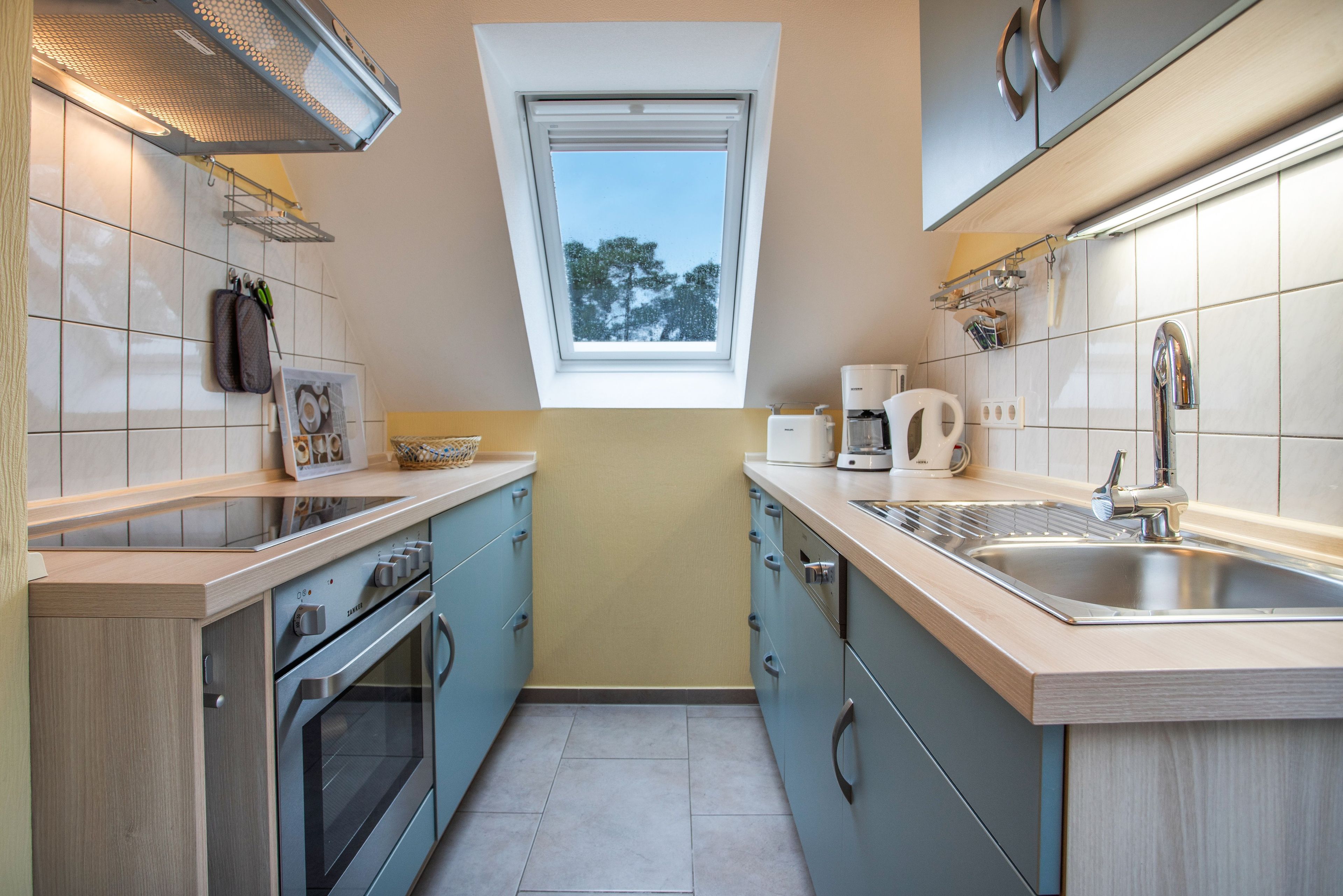 A compact kitchen with a built-in oven, a coffee maker, and a window above the sink.