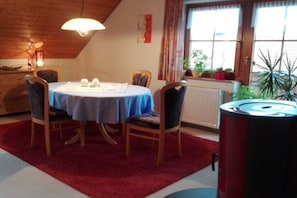 A dining area with a table set for four, surrounded by chairs, a red carpet, and a window with curtains. - Holiday apartment with 1 bedroom (Bonndorf)