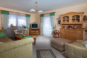 Ein Wohnzimmer mit Sofa, Sessel, Holzschrank, Fernseher und einer dekorativen Spindelschwengel.