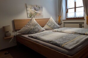 Ein Doppelbett mit Holzabdeckung, zwei Nachttische, eine Wandlampe und ein Fenster mit Vorhängen.