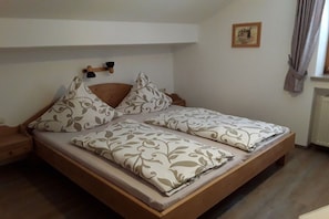 A single bed with a wooden frame, two pillows with a leaf pattern, a bedside table, and a wall-mounted light fixture. - Holiday apartment with 1 bedroom (Bischofswiesen)