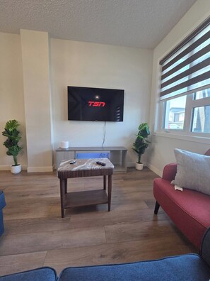A modern living room with a flat-screen TV mounted on the wall, a wooden coffee table, a red sofa, and two potted plants. - Spacious Family House in Edmonton - Perfect for a Comfortable Stay (Edmonton)