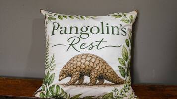 Een vierkant kussen met een pangolin-illustratie en de tekst 'Pangolin's Rest' op een effen muur.