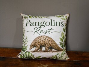 En fyrkantig kudde med en illustration av ett skölddjur och texten ”Pangolin’s Rest” på en enkel vägg.