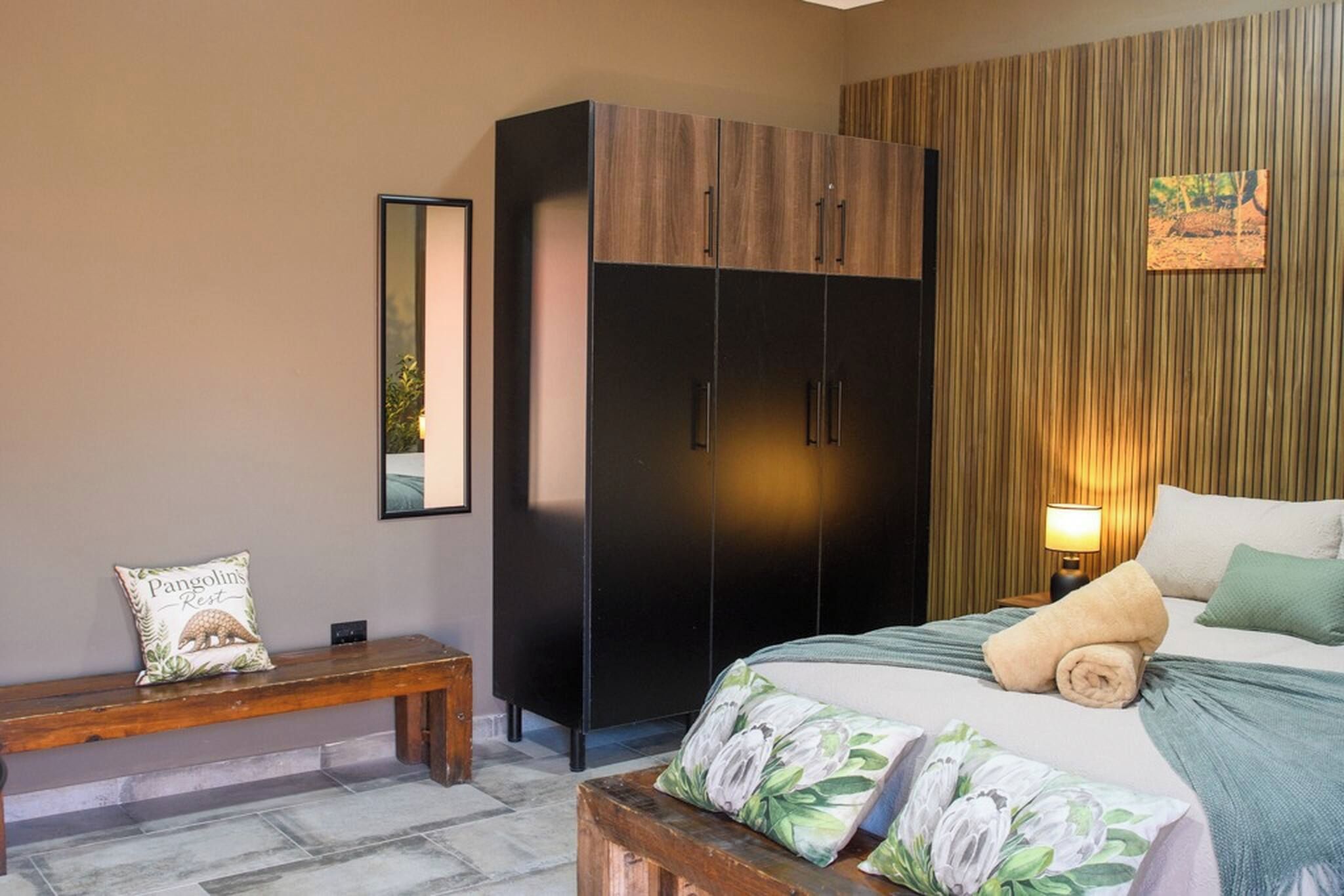 Een slaapkamer met een bed, een bankje, een kledingkast en een wandlamp.