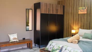 Een slaapkamer met een bed, een bankje, een kledingkast en een wandlamp.
