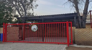A gated entrance with a red metal fence, a brick wall, and a covered area with a roof. - Pangolin's Rest - Unit 1 (Phalaborwa)