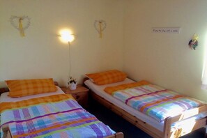 Ett sovrum med två enkelsängar, var och en med en orange kudde och en färgglad randig filt. Det finns ett nattduksbord med en lampa och en liten växt.