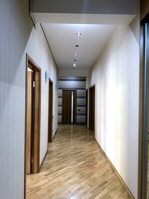 Un couloir doté d’un plancher en bois et de portes des deux côtés, qui mène à une pièce avec un mur à rayures et un luminaire au plafond.