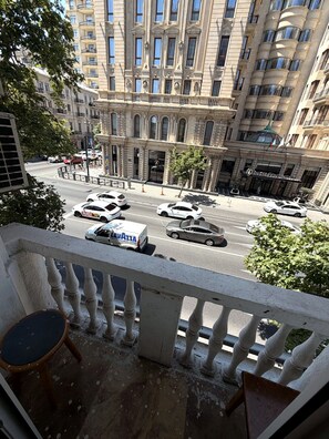 A balcony with a view of a busy street, cars, and a building with classical architecture. - Baku Bulvar 3BR Luxury Apartment (Baku)