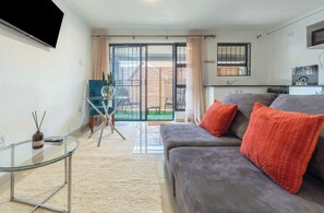 A modern living room with a grey sofa, a glass coffee table, and a view of a balcony. - Solar powered home with water always (Edenvale)