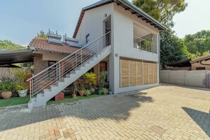 A modern two-story house with a staircase leading to the upper floor, a covered outdoor area, and potted plants. - Solar powered home with water always (Edenvale)