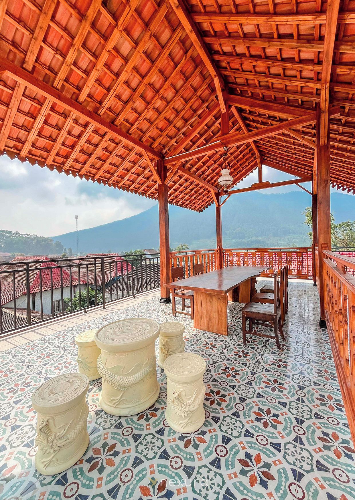 Un espacio de estar al aire libre techado, con mesa y sillas, un suelo decorativo y vistas a un paisaje montañoso.