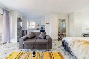 A modern hotel room with a grey sofa, a bed, a small kitchen area, and a bathroom with marble tiles. - M&M Uphill Solar powered home with running water cold and hot (Edenvale)