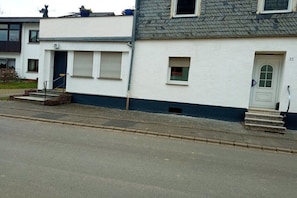 Ein zweistöckiges Wohngebäude mit weißer Fassade, Hausnummer 29, mit einer Haustür, einem kleinen Fenster und einer Treppe, die zum Eingang führt.